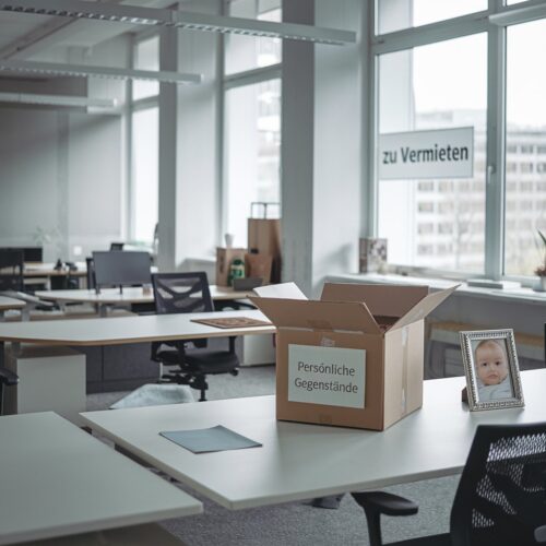 Leeres Büro mit "Zu Vermieten"-Schild, leeren Schreibtischen und einem Bild eines Babys.